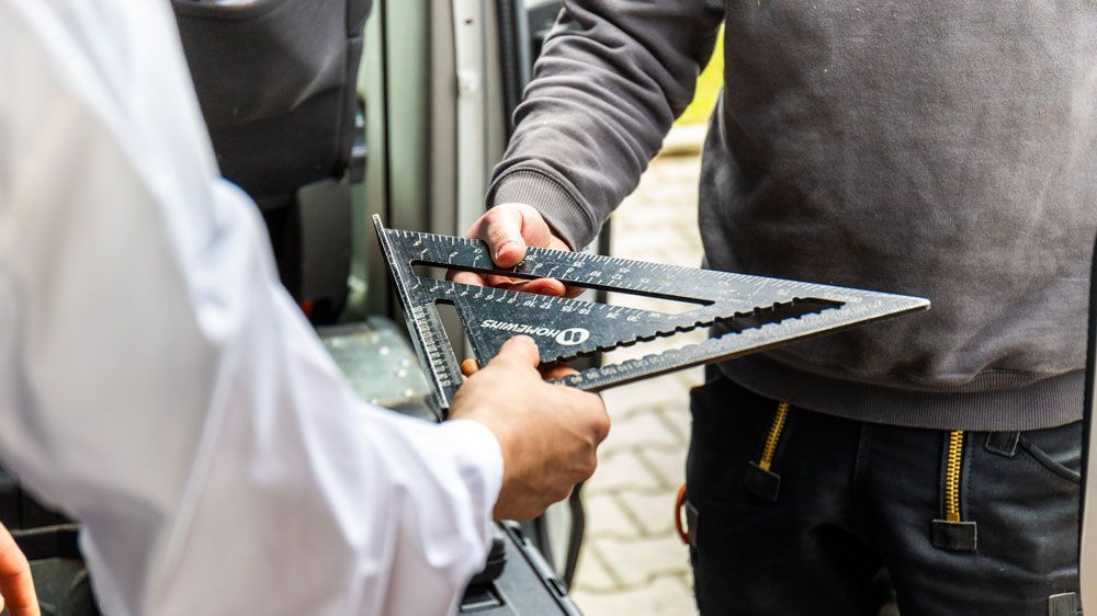 Ein Mann hält ein Lineal in der Hand und steht neben einem anderen Mann.