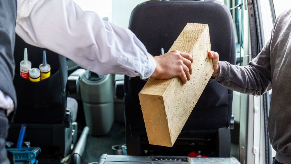 Ein Mann hält in einem Auto ein Stück Holz.