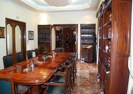 Comedor con una mesa larga de madera, sillas y estanterías empotradas. Botelleros a la vista.