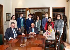 Grupo de personas vestidas de traje alrededor de una mesa de madera en un entorno de oficina, sonriendo y mirando a la cámara.