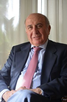 Hombre de traje, sentado en un interior, con las manos entrelazadas. Lleva una corbata rosa estampada y sonríe levemente.