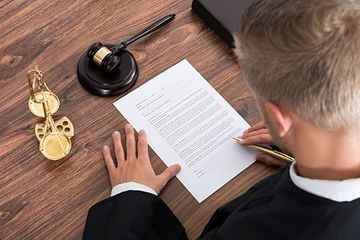 Juez revisando un documento con un mazo y una balanza de la justicia sobre un escritorio de madera.