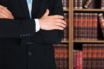 Hombre de traje con los brazos cruzados delante de una estantería llena de libros de derecho.