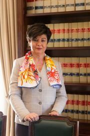 Una mujer con un blazer ligero y una bufanda estampada está parada frente a una estantería.