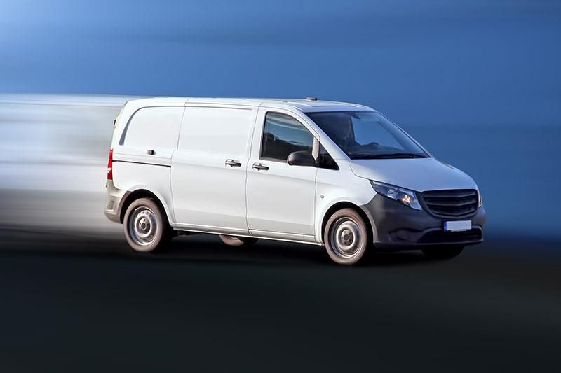 Ein weißer Lieferwagen fährt schnell auf einer Straße.