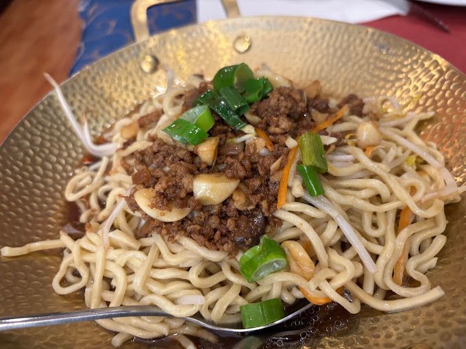Un tazón de fideos con carne y verduras y una cuchara dentro.