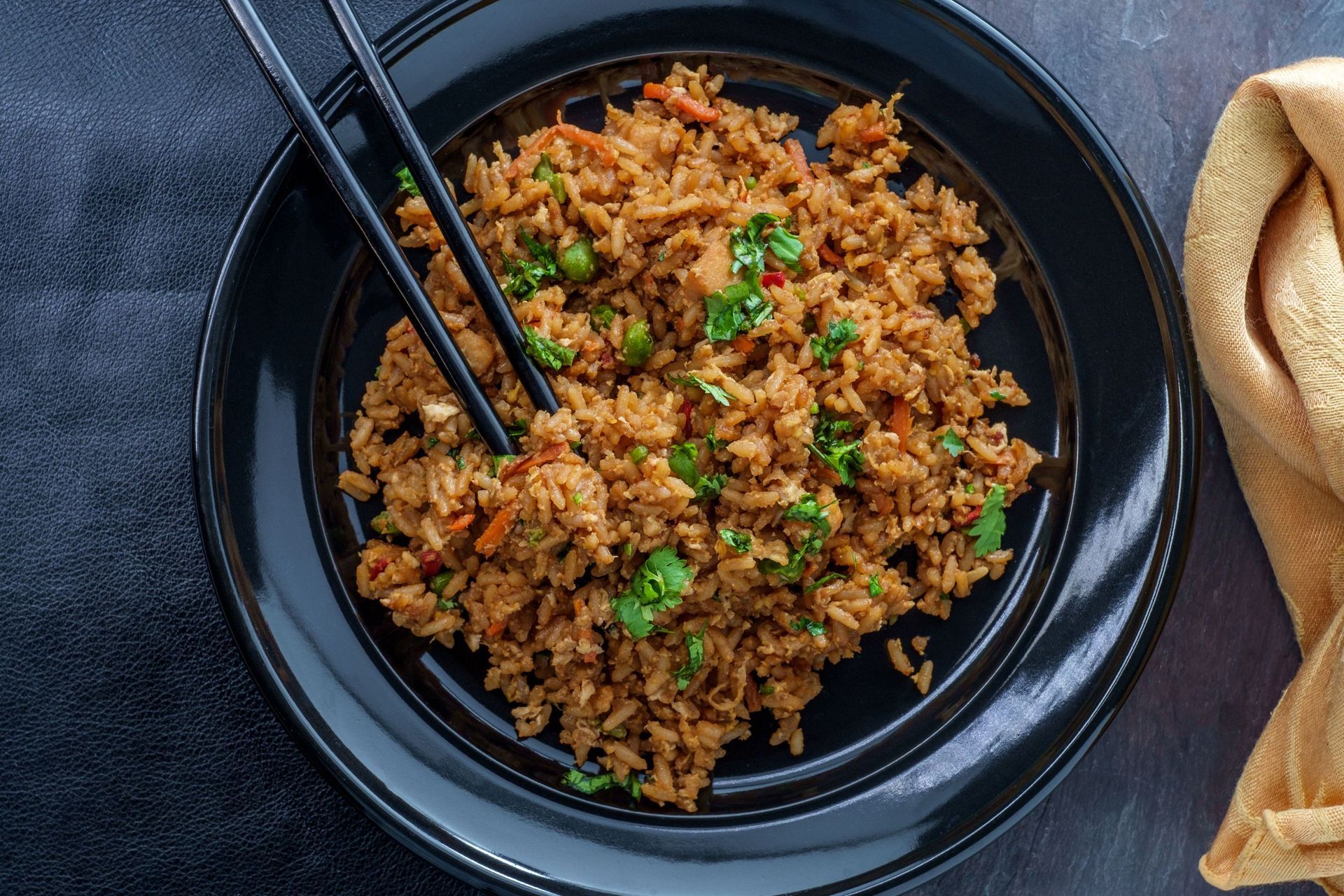 Un plato negro cubierto con arroz y palillos sobre una mesa.