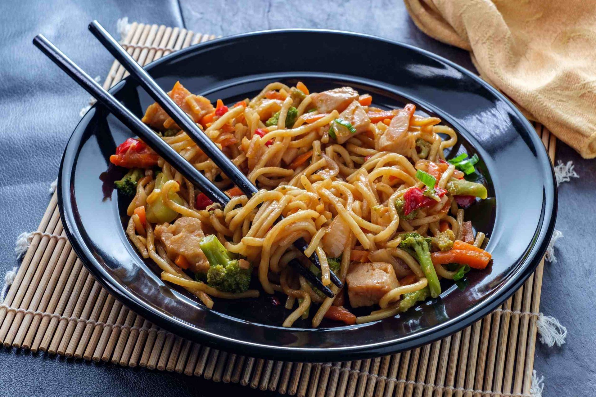 Un plato negro cubierto con fideos y verduras con palillos.