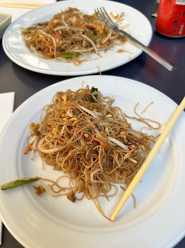 Dos platos de fideos con palillos y un tenedor sobre una mesa.