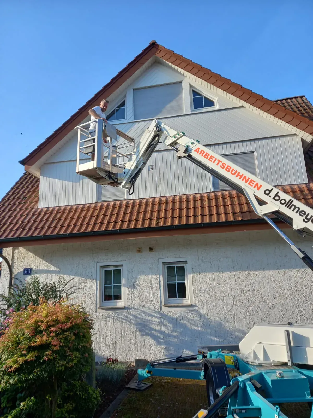 Ein Mann streicht mit einem Kran die Seite eines Hauses.