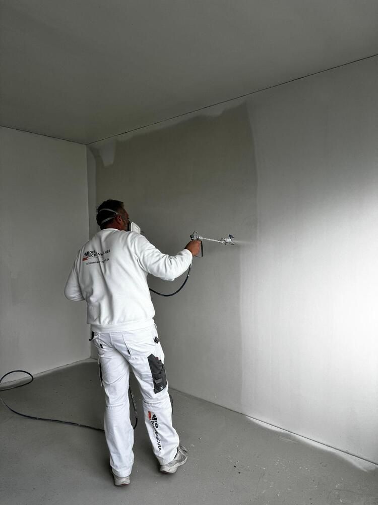 Ein Mann sprüht Farbe auf eine Wand in einem Raum.