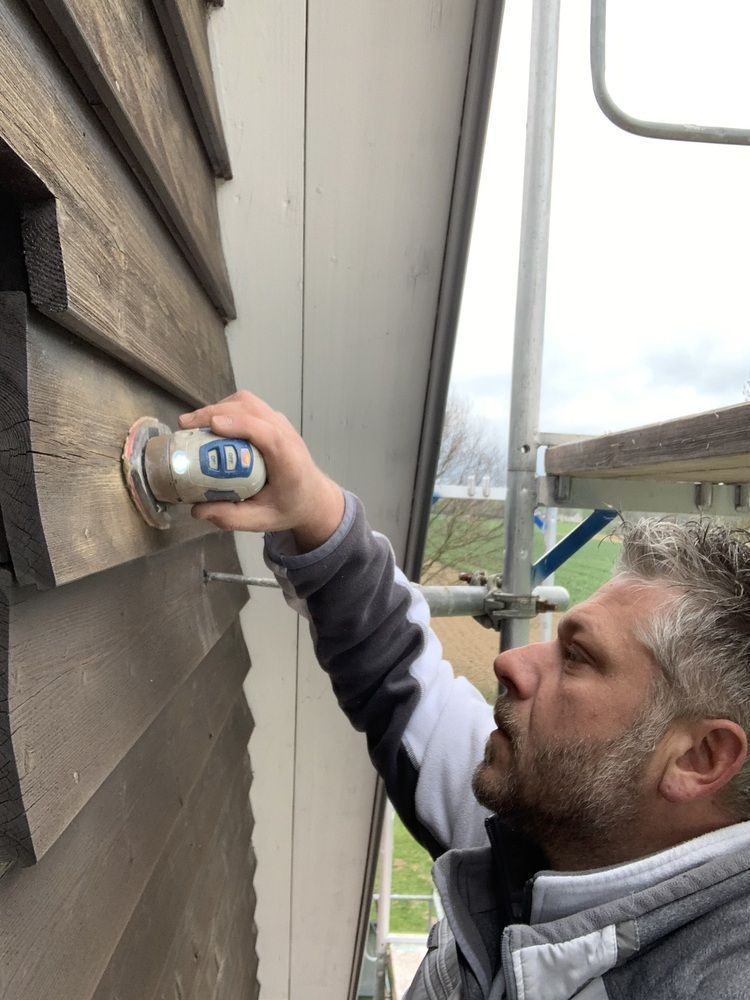 Thomas Neusel arbeitet mit einer Dose Klebstoff in der Hand an einer Holzwand.