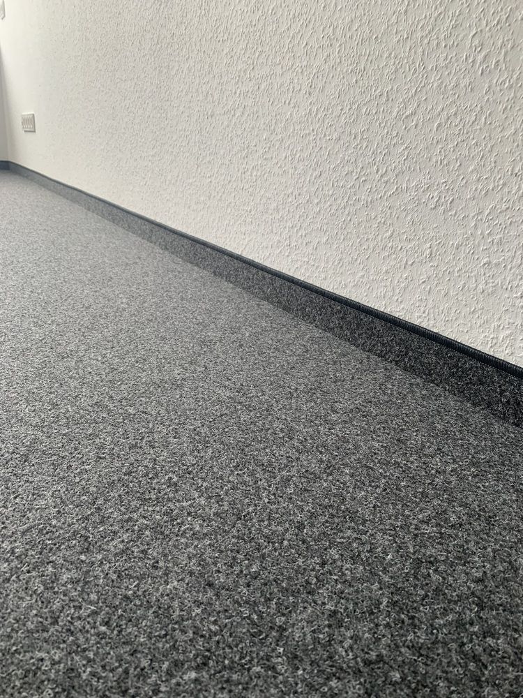 Ein Raum mit einem grauen Teppich und einer weißen Wand.