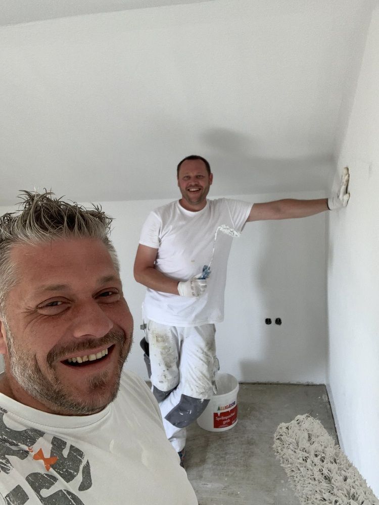 Thomas Neusel und sein Team streichen gemeinsam eine Wand und lächeln.