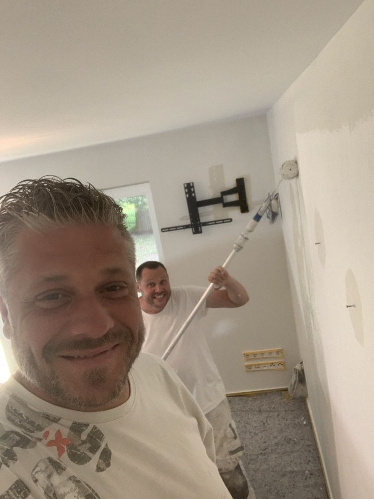 Thomas Neusel und sein Team streichen gemeinsam eine Wand und einer hält eine Farbrolle.