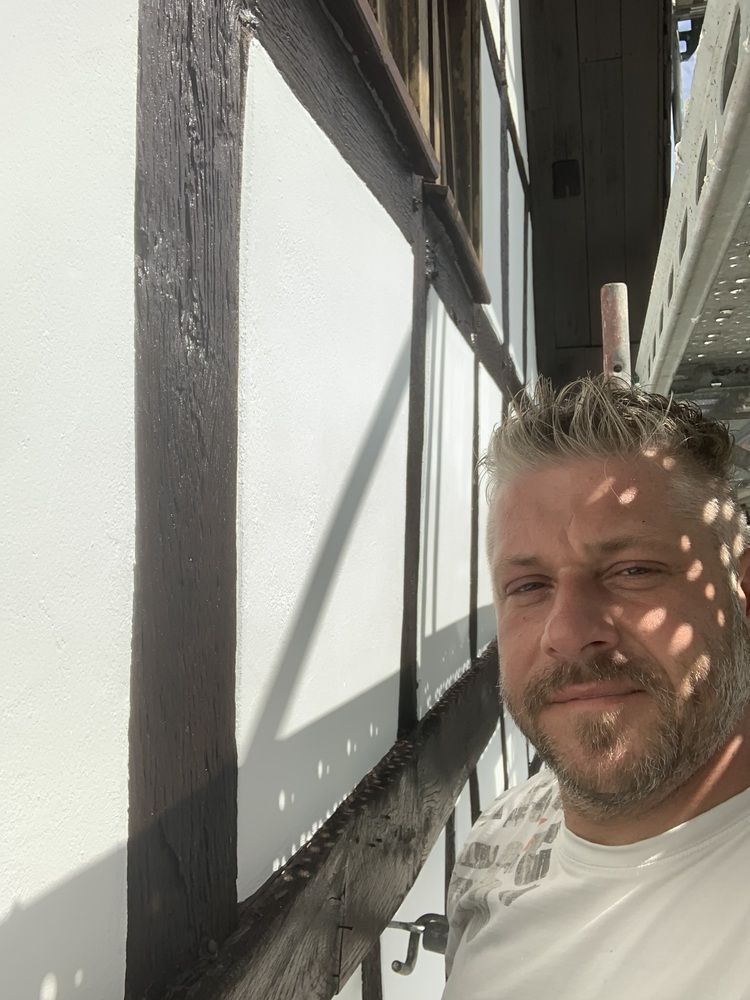 Ein Mann mit Bart steht vor einer weißen Wand.