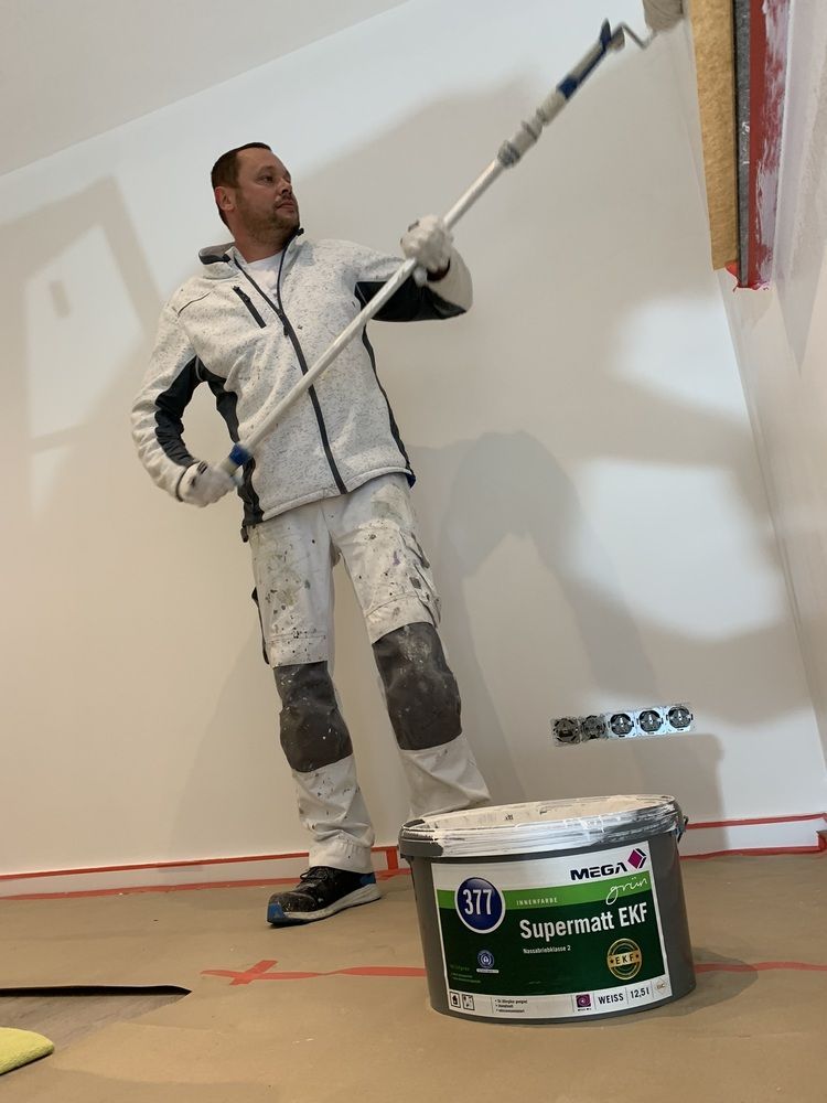 Ein Mann streicht eine Wand mit einer Farbrolle.
