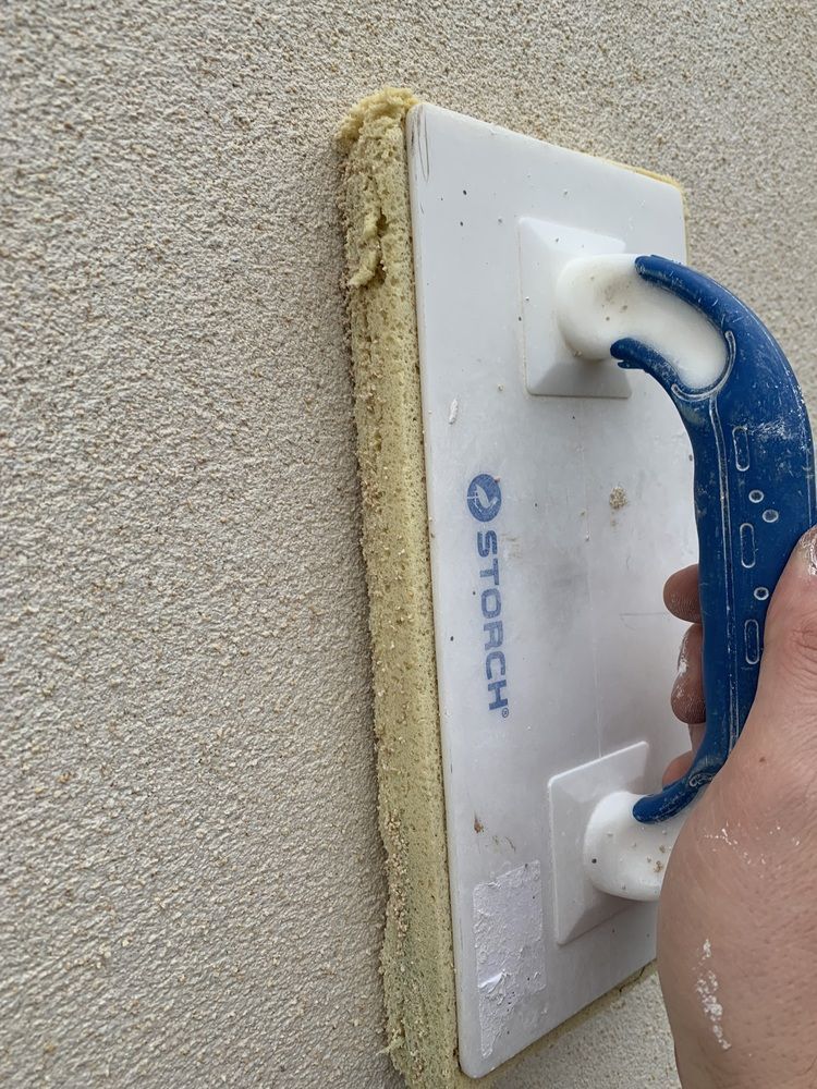 Eine Person hält einen Styroporschwamm gegen eine Wand.