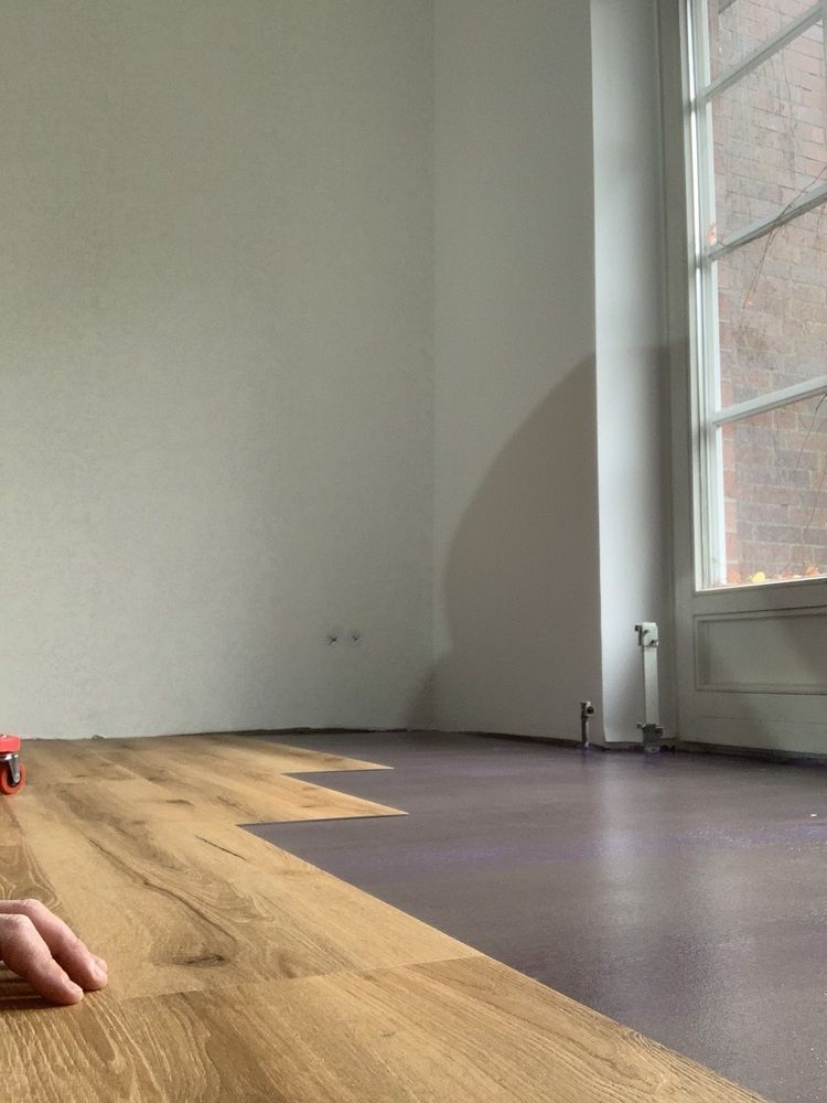 Eine Person liegt auf einem Holzboden in einem leeren Raum.