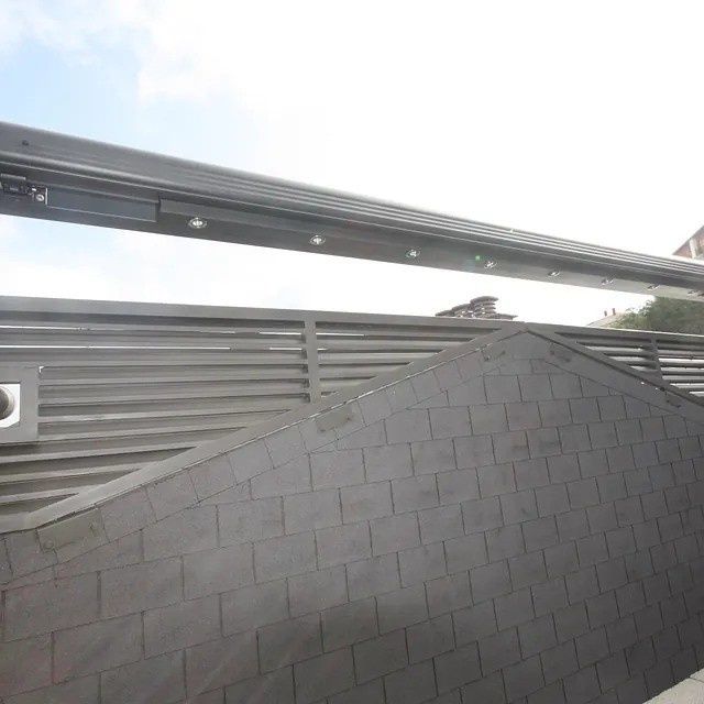 Tejado de tejas grises en primer plano con rejilla de ventilación y puente o barandilla elevada encima.