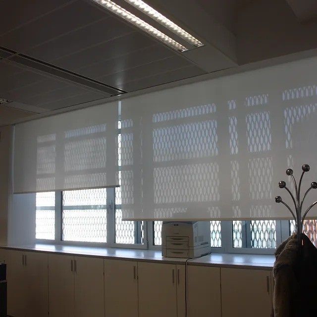 Interior de una oficina con ventanas cubiertas por persianas y un perchero en primer plano.