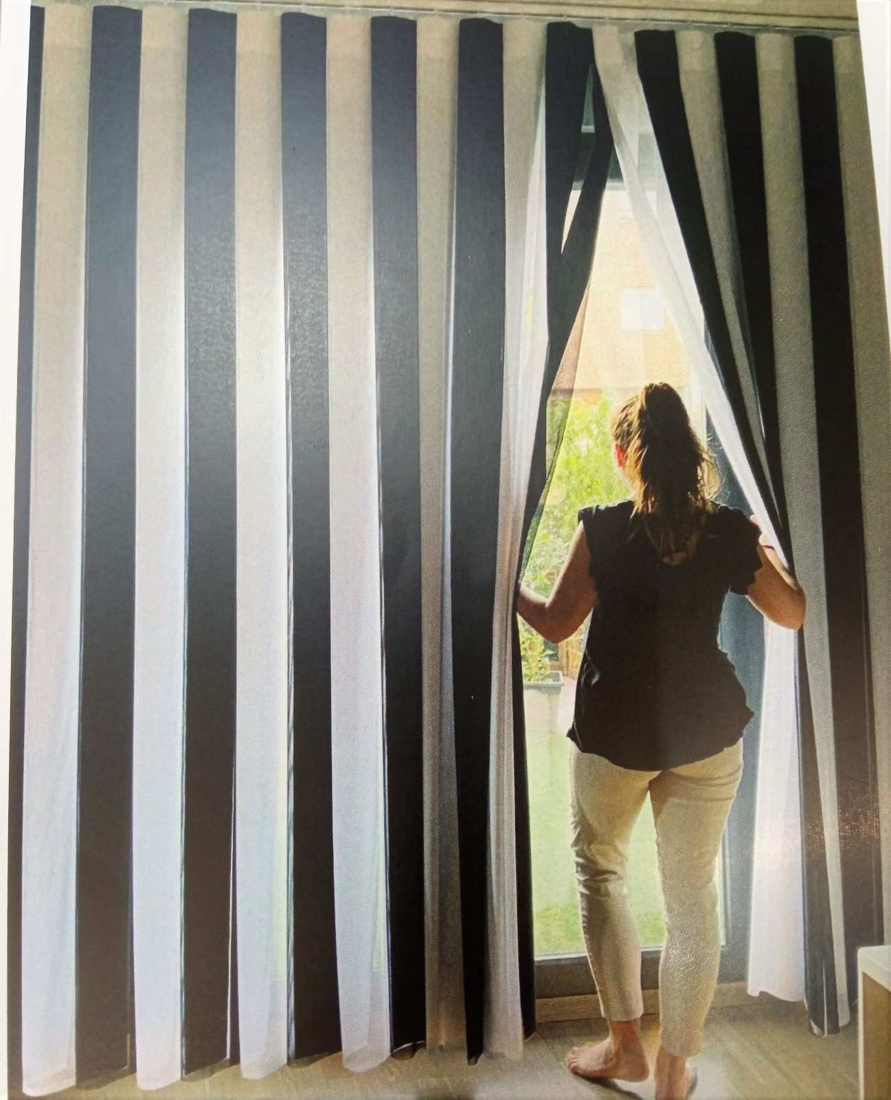 Una persona aparta unas cortinas a rayas para mirar hacia una ventana luminosa.