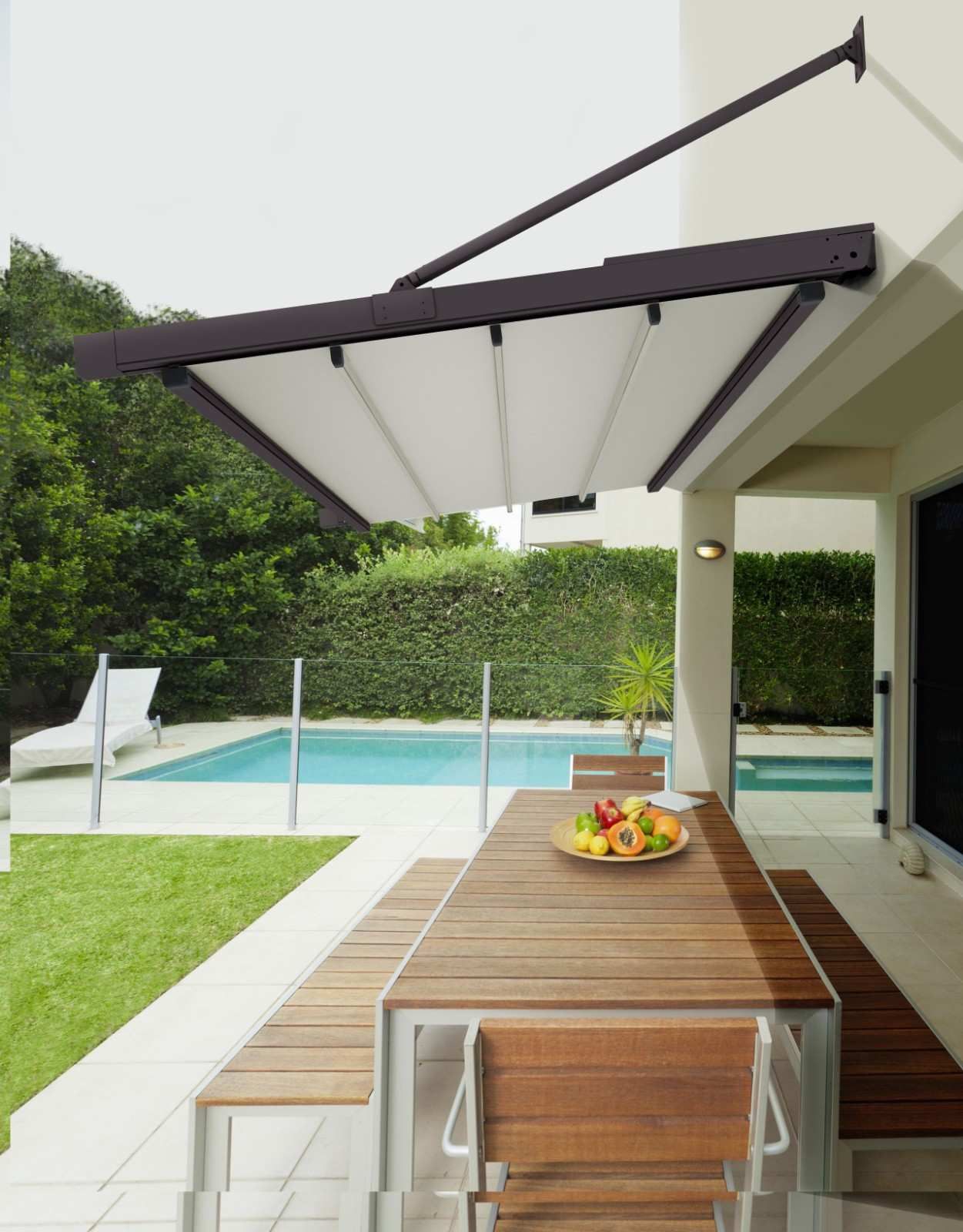 Patio moderno con toldo retráctil, mesa de comedor de madera y una piscina al fondo.