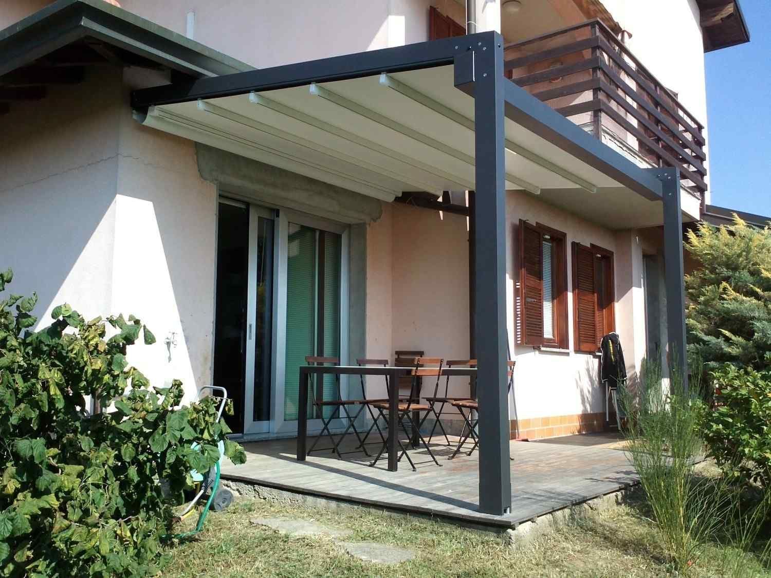 Patio con mesa y sillas junto a una casa, bajo un balcón cubierto con contraventanas de madera.