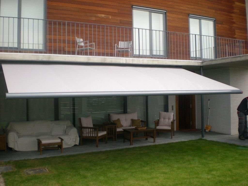 Patio con toldo blanco, asientos al aire libre y balcón en la planta superior de una casa adosada de ladrillo.