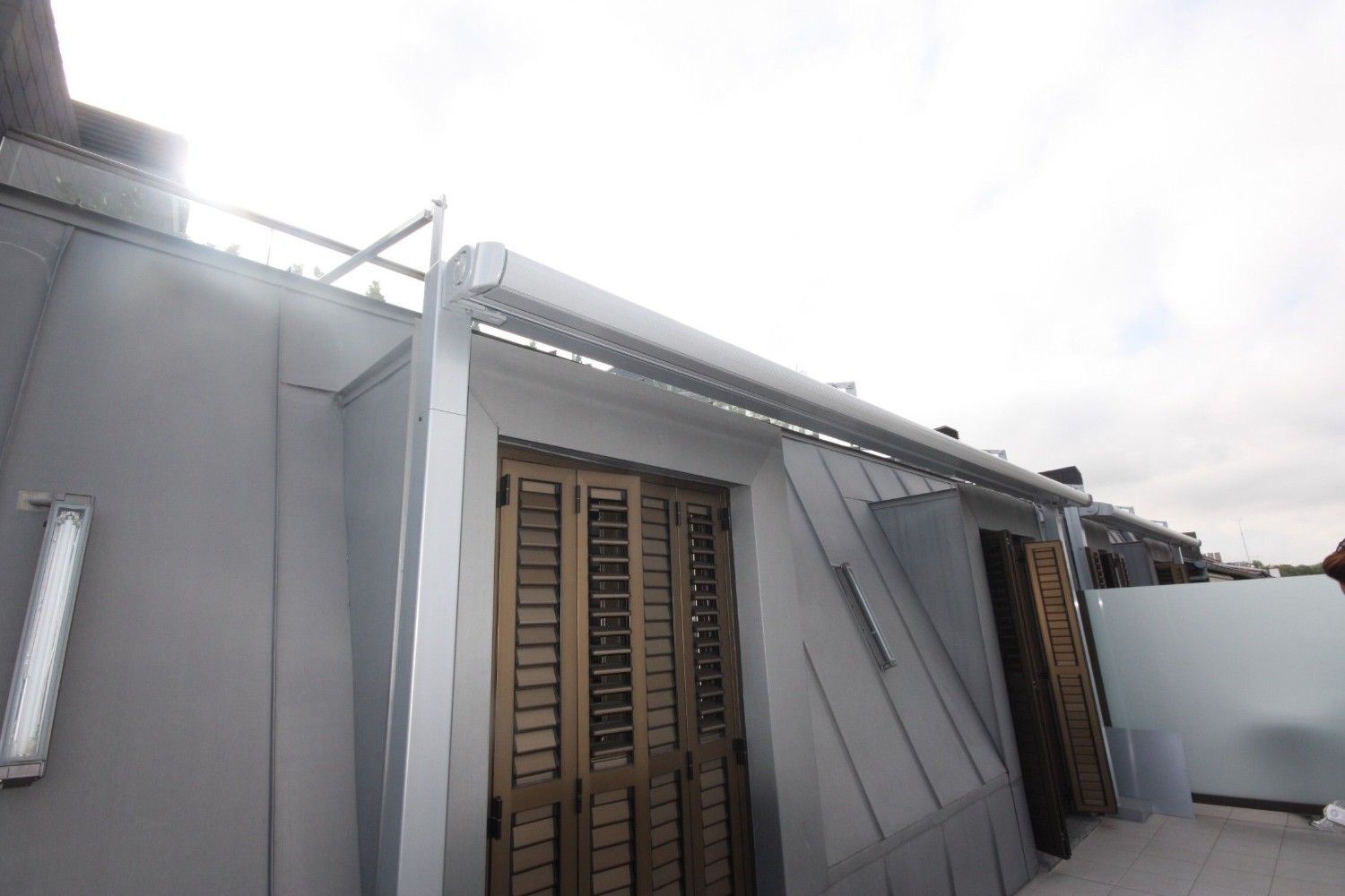 Exterior de una casa gris con contraventanas de madera y una pared blanca bajo un cielo brillante.