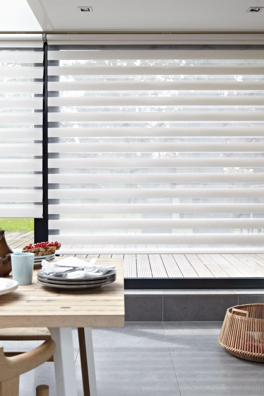 Patio moderno con mesa de madera, vajilla, cesta de mimbre y persianas horizontales blancas.