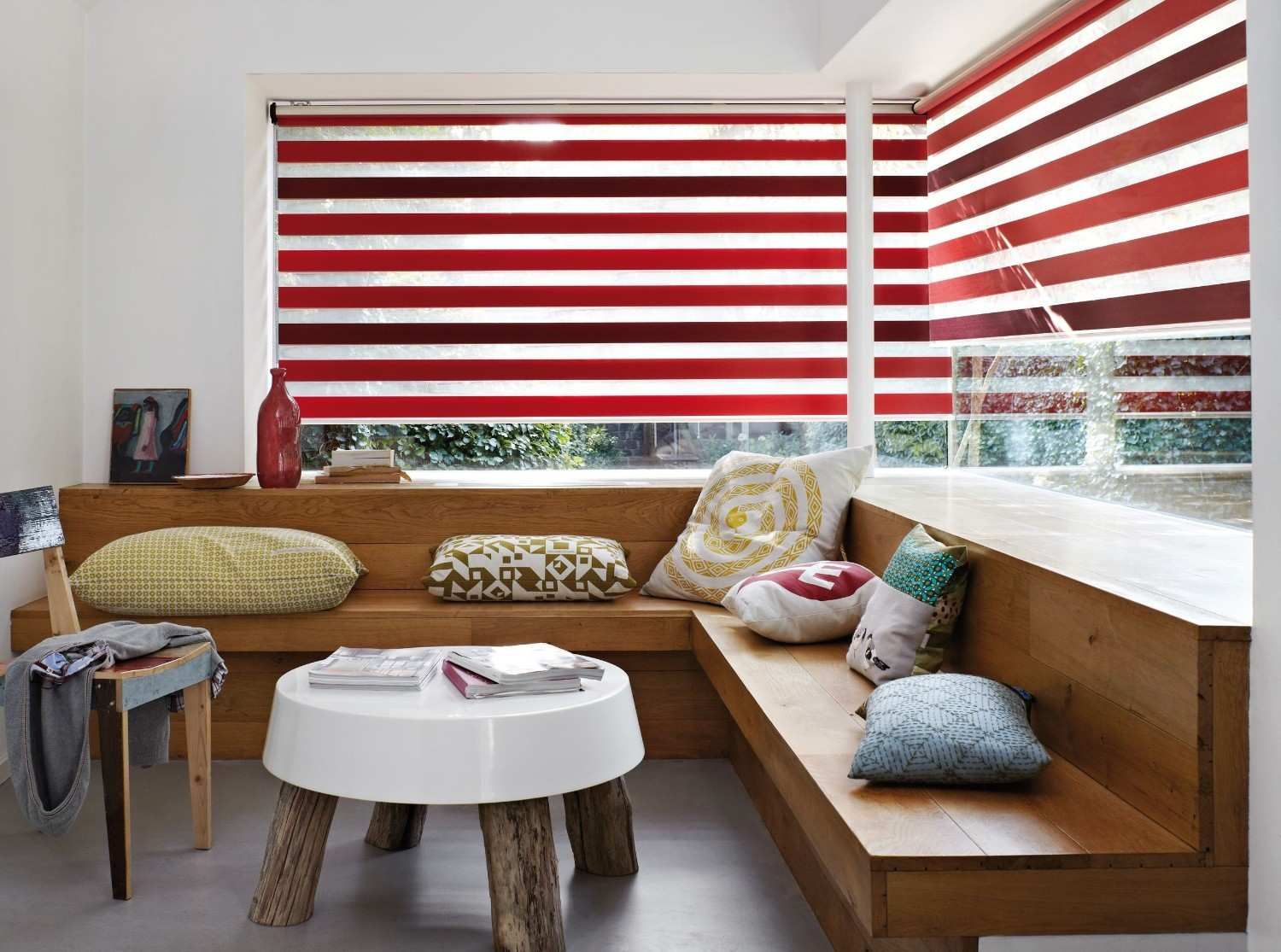 Acogedor salón de madera con persianas a rayas rojas y blancas, bancos, cojines y una pequeña mesa blanca.