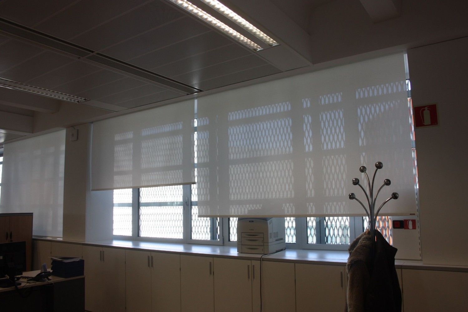 Interior de oficina con persianas cerradas, armarios, luces de techo y un perchero.