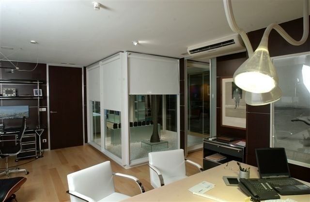 Interior de oficina moderno con escritorios, sillas, grandes ventanales y tabiques de cristal.