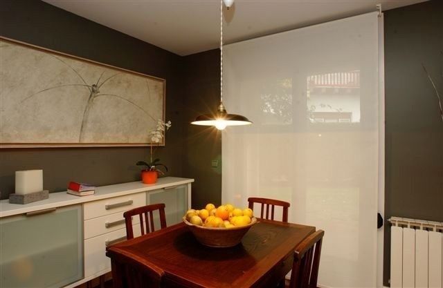 Comedor con mesa de madera oscura, frutero, lámpara colgante y aparador contra una pared gris.