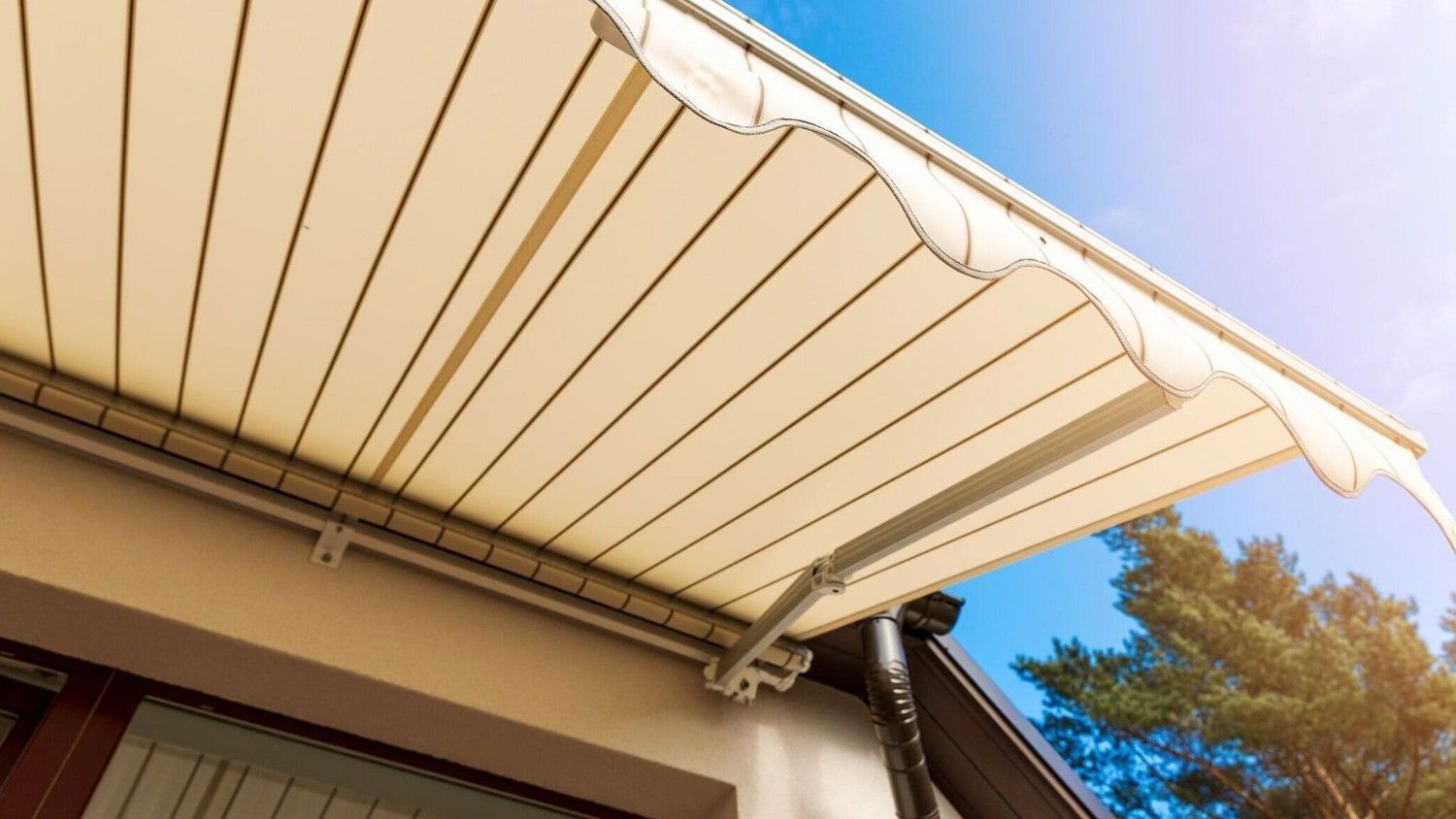 Toldo retráctil beige que se extiende sobre el tejado de una casa contra un cielo azul.