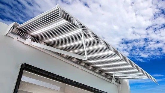 Un toldo blanco ondulado se extiende desde el tejado de un edificio contra un cielo azul y nubes.