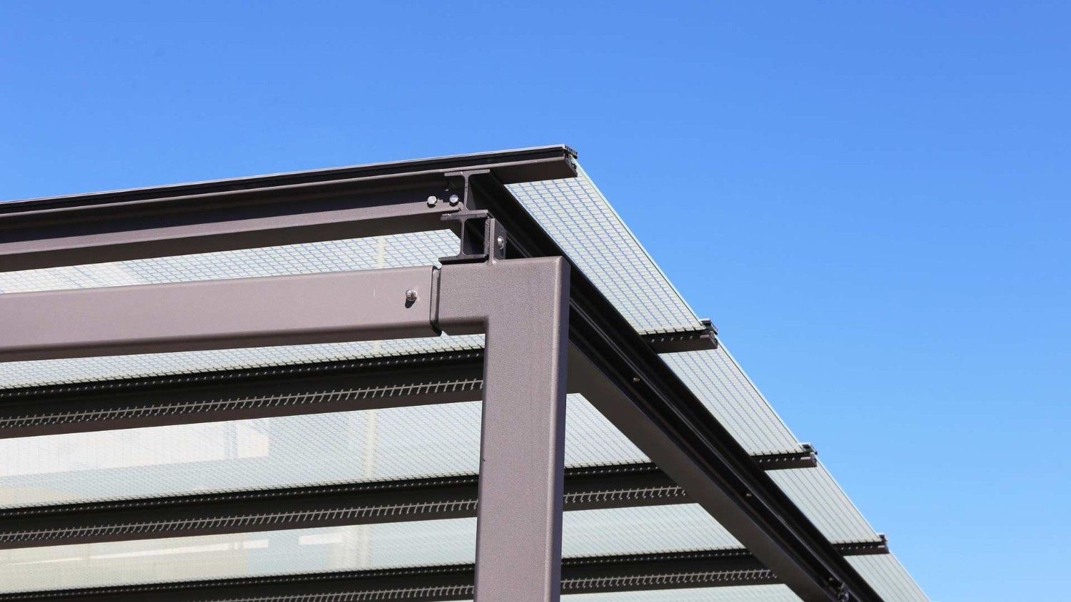 Primer plano del tejado de un edificio moderno con vigas metálicas y paneles translúcidos contra un cielo azul.