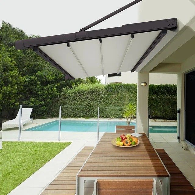 Patio moderno con toldo retráctil, mesa de madera, piscina y jardín paisajístico.
