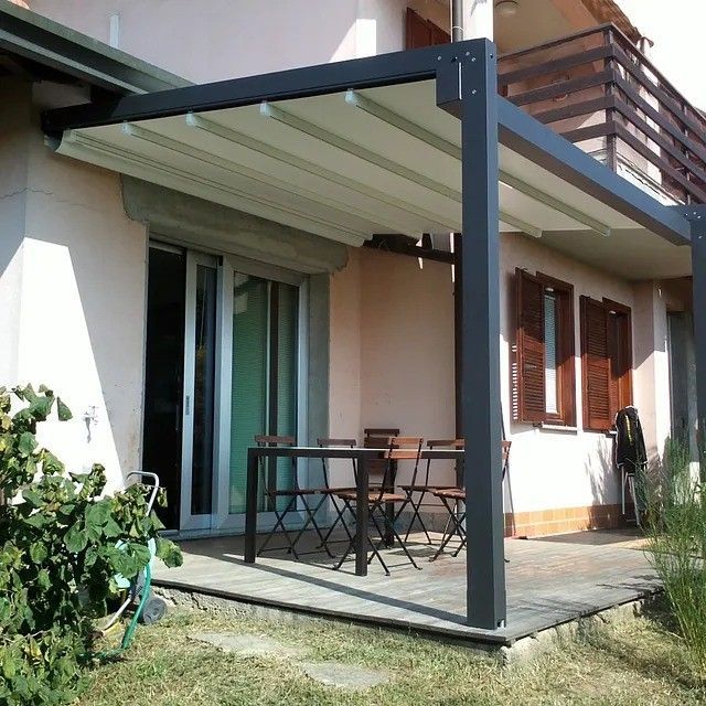 Patio cubierto con mesa y sillas de exterior junto a una casa, con postes de soporte de color gris oscuro y toldo retráctil.