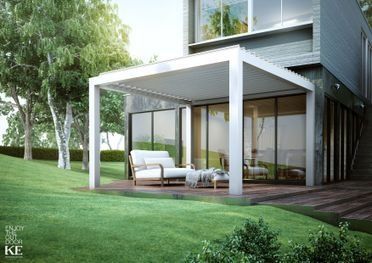Patio de casa moderna con pérgola blanca, asientos al aire libre y grandes puertas de cristal con vistas a un césped verde.