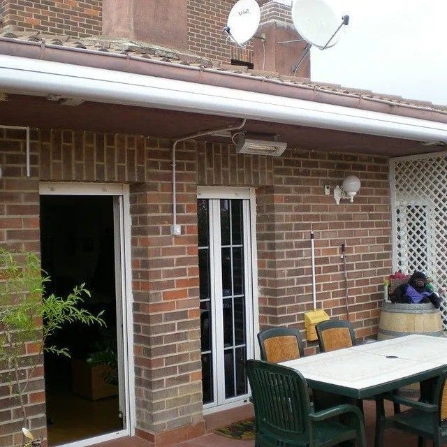 Patio de ladrillo con mesa y sillas de exterior junto a una casa de ladrillo, una puerta blanca y antenas parabólicas.