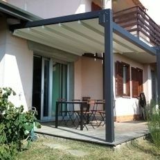 Patio moderno con toldo, mesa y sillas de exterior junto a una casa y balcón.
