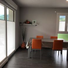 Comedor moderno con sillas naranjas, una mesa de madera y puertas corredizas de vidrio a la izquierda.