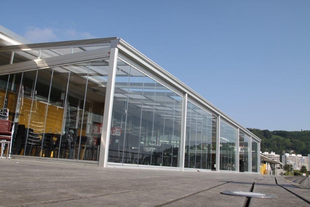 Edificio moderno de cristal con techo inclinado y plaza abierta en un día soleado.