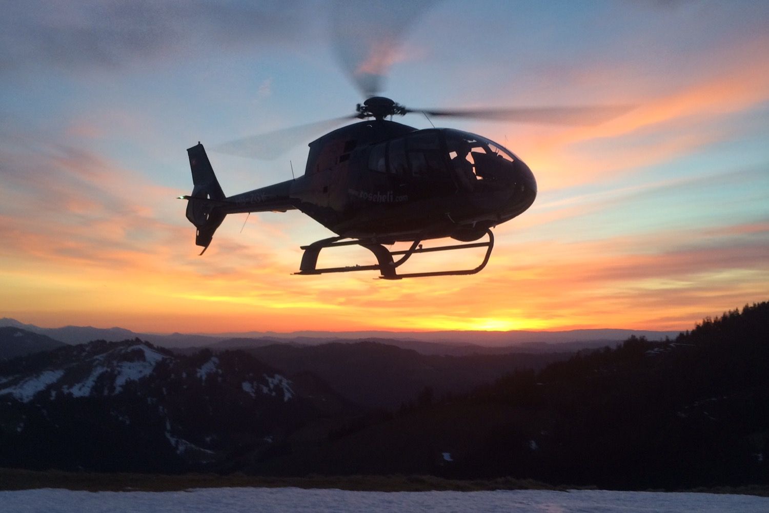 Ein Hubschrauber fliegt bei Sonnenuntergang über einem Berg