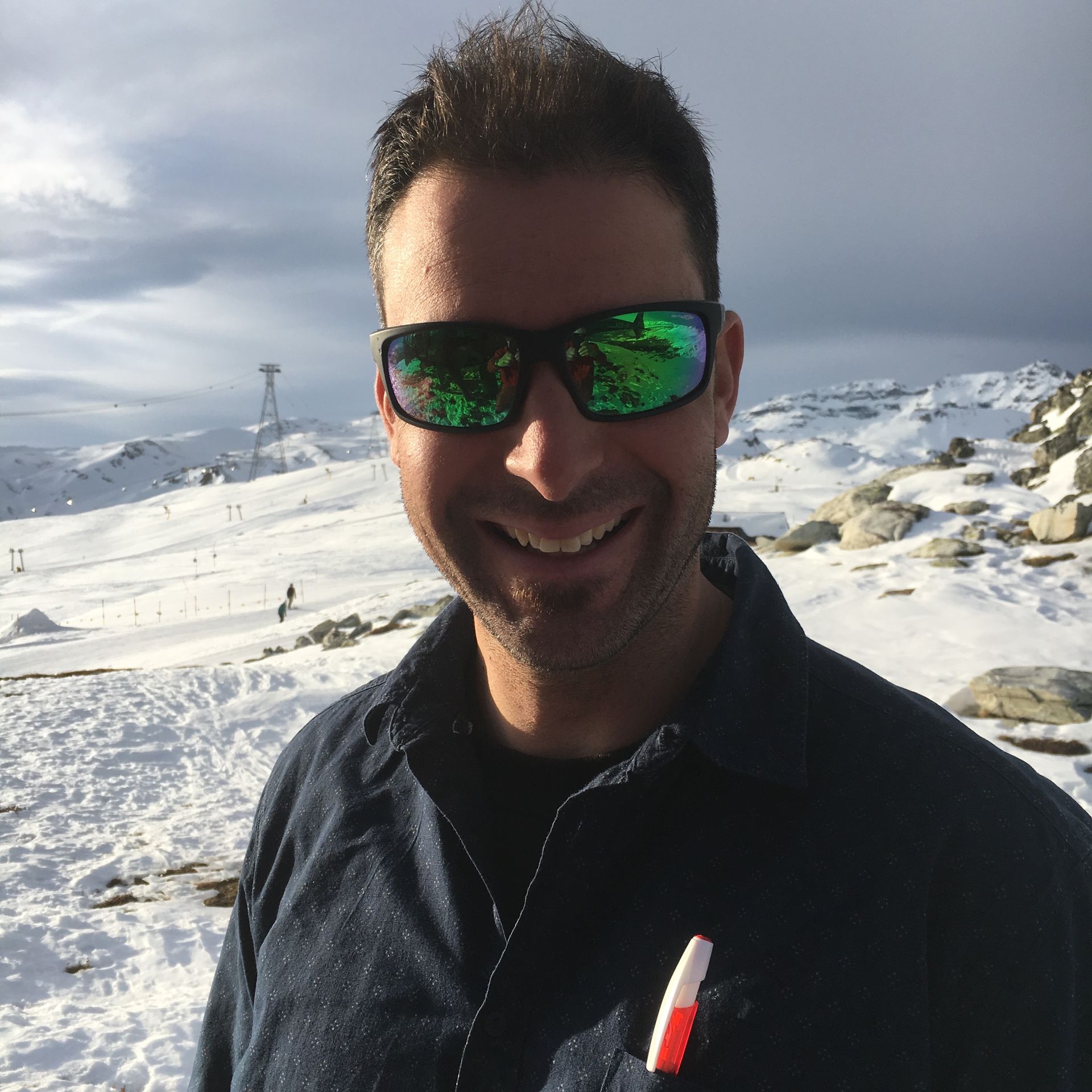 Ein Mann mit Sonnenbrille lächelt vor einem schneebedeckten Berg