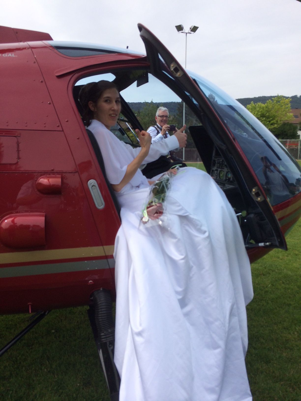 Eine Frau im Brautkleid sitzt im Cockpit eines roten Hubschraubers