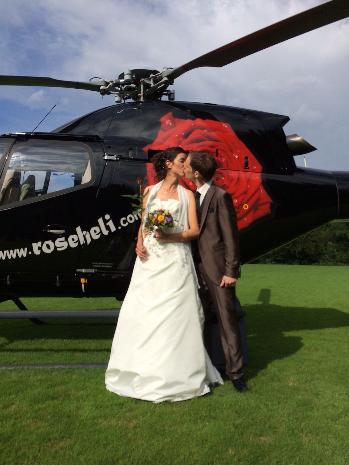 Braut und Bräutigam küssen sich vor einem Roseheli-Hubschrauber