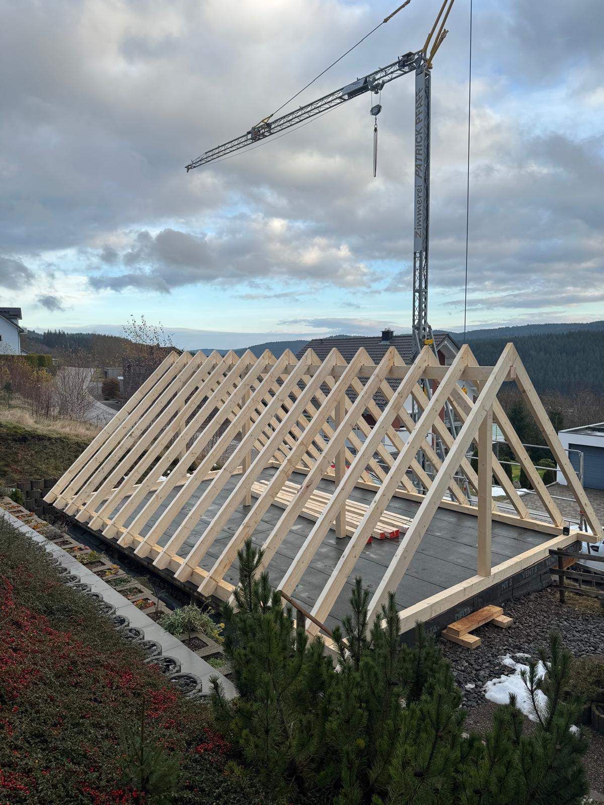 Eine Baustelle mit einem Kran, der ein Stück Holz anhebt, Zimmerei Patrick Pfaff